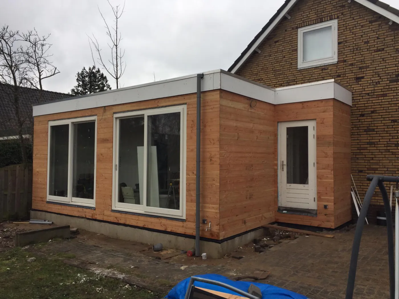 Opgeleverde aanbouw met houten gevelbekleding, plat dak en grote schuifpui door PersianTop